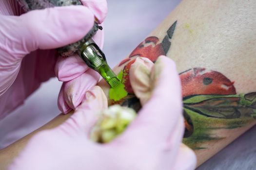Close-up of a female artist making a color tattoo on the leg of a young girl. Tattoo artist stuffs a ladybug on a girl's leg, tattoo for a girl.