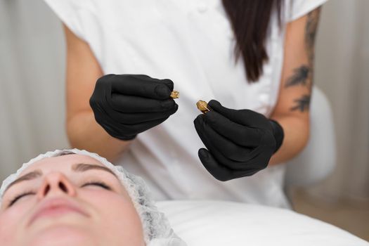 Close-up of a beautician doctor in black sterile gloves opens an ampoule with hyaluronic acid before the rejuvenation procedure.