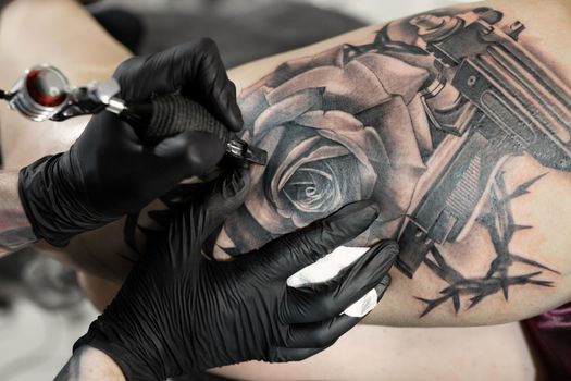 Close up image of the bearded tattoo male artist makes a tattoo on a female leg.