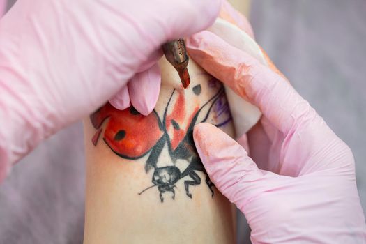 Needle tattoo machines inject a red ink into the skin of a girl. Close-up of the process of applying the tattoo on the skin.