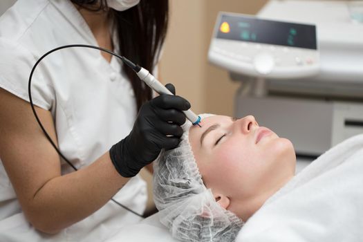 Therapist beautician makes a laser treatment to young woman's face at beauty SPA clinic. Close-up process of laser removal of blood vessels from the skin.
