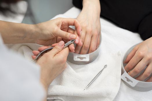 Nail Salon. Closeup Of Female Hand With Healthy Natural Nails Getting Nail Care Procedure. Hands Removing Cuticles With Professional Nail Tool, Metal Clippers. Beauty Manicure.