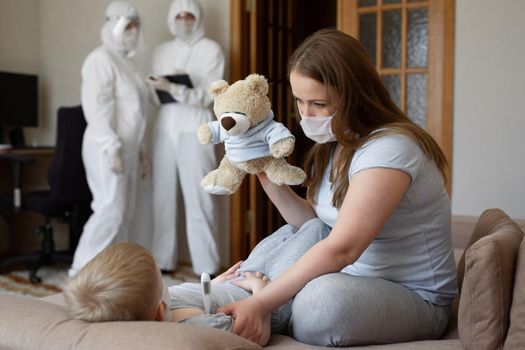 Mom measures baby's temperature. Doctors in protective suits at sick patients at home. Coronavirus, covid-19