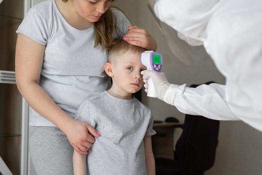 Pediatrician or doctor checks elementary age boy's body temperature using infrared forehead thermometer gun for virus symptom - epidemic coronavirus outbreak concept