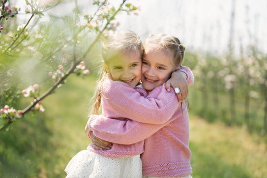 Happy two twin sisters are hugging against the background of a green blossoming apple orchard
