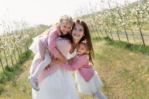 Happy family in the Apple orchard. Mom and two twin daughters have fun and hug
