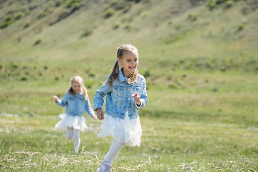 Two little twin sisters run and spin in the meadow