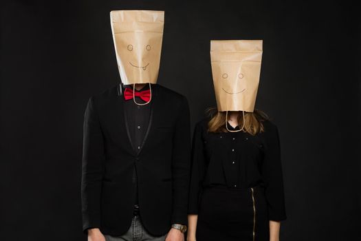 Young couple with bags over heads on black background.