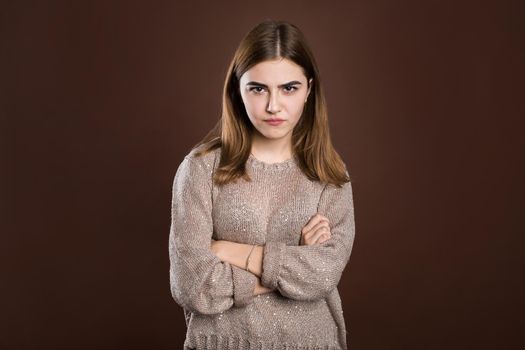 Portrait of beautiful girl frowning her face in displeasure, wearing loose long-sleeved sweater, keeping arms folded. Attractive young woman in closed posture