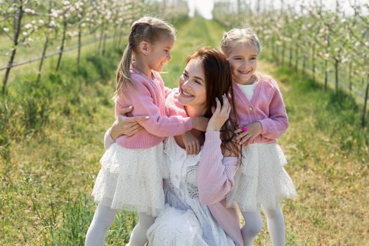 Portrait of a mother and her twin daughters in a blooming Apple orchard