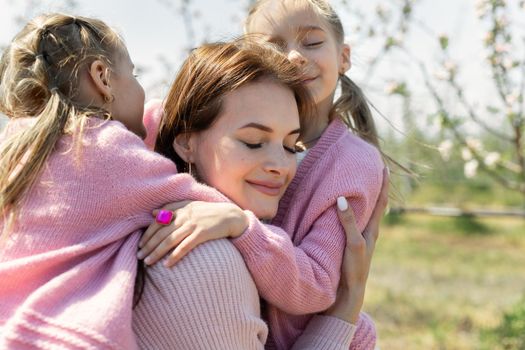 Close-up portrait of a young mother and her twin daughters hugging in an Apple orchard
