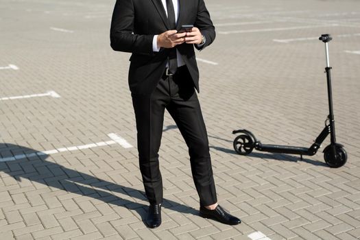 Young handsome businessman in a suit rides an electric scooter and looks at the phone
