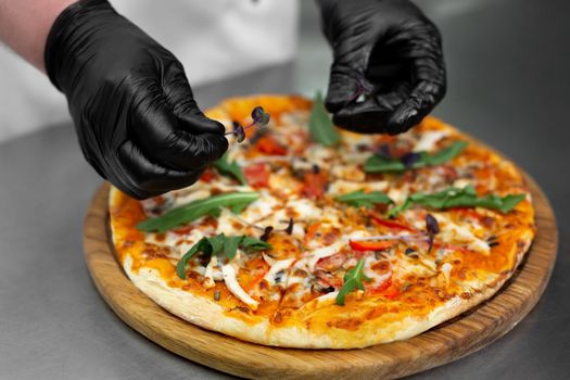 Close-up of the chef's gloved hands decorating pizza with greens, arugula