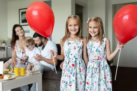 Two twin sisters pose with balloons in the background of the family. who eats breakfast in a hotel room