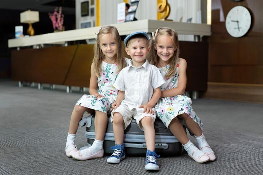 Twin sisters and brother sitting on a suitcase in a hotel