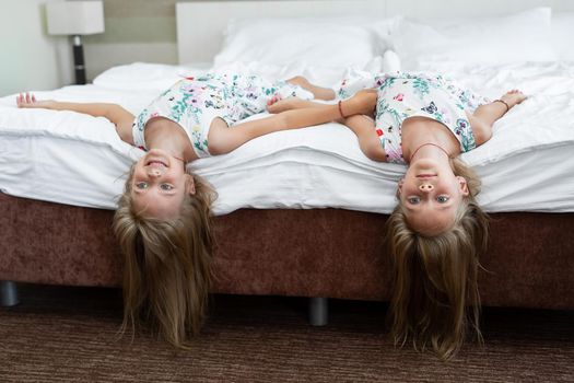 Two twin sisters are lying on the bed upside down