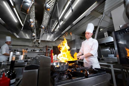 Chef cooking with flame in a frying pan on a kitchen stove.