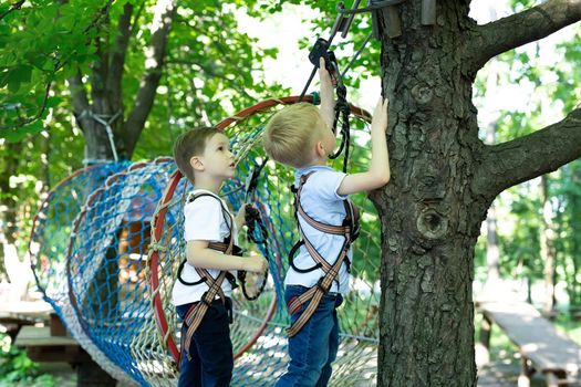 A little boy helps his friend with equipment in a rope park