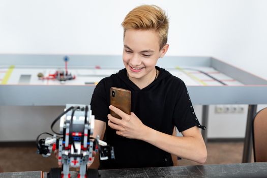 Student builds a robot constructor from plastic parts programmed on a computer during a robotics lesson at school and takes pictures on the phone.