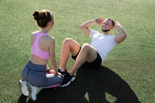 Man and a woman pump their abs in the park on the grass.