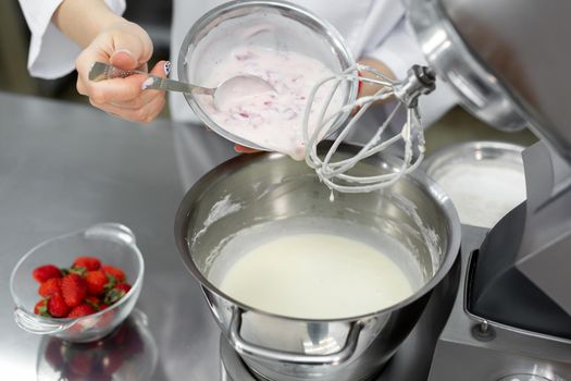 Pastry chef adds cream and strawberries to the bowl of the mixer and knead the dough