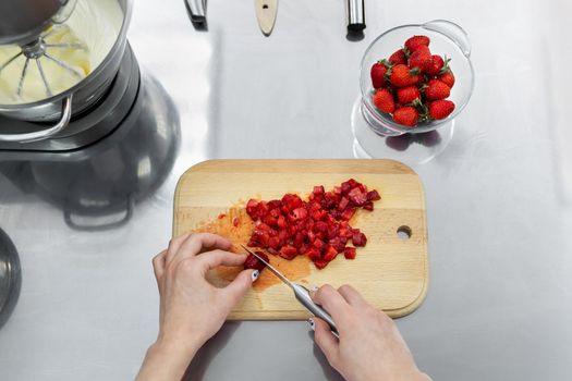 Close up of woman hands cutting strawberries on cutting board.