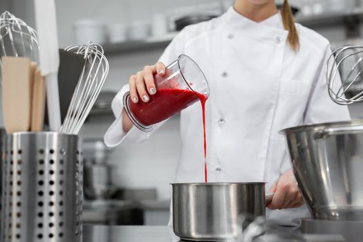 Pastry chef pours strawberry puree into a saucepan