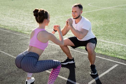 Young sports couple trains at the stadium in the summer at sunset, warm up and squat. Sport. Fitness.