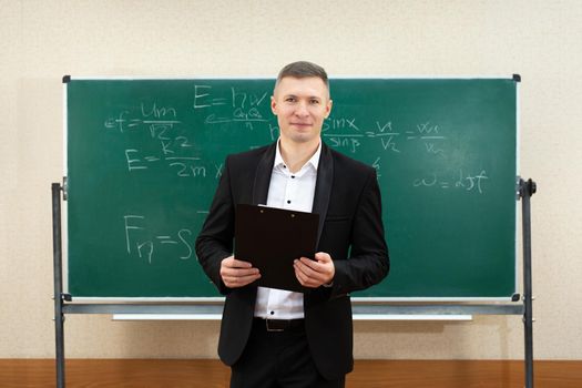 The male teacher used white chalk to write on the blackboard to teach students in a class