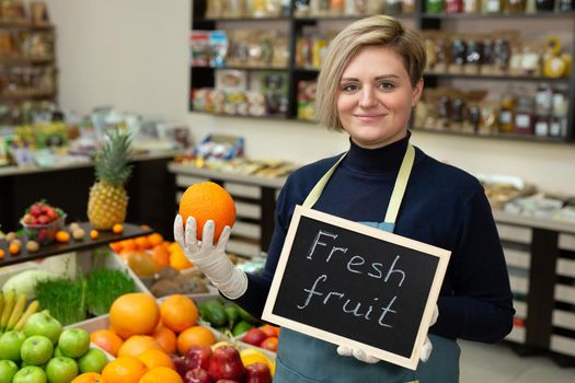 Portrait of a young saleswoman with a sign in her hands fresh fruit
