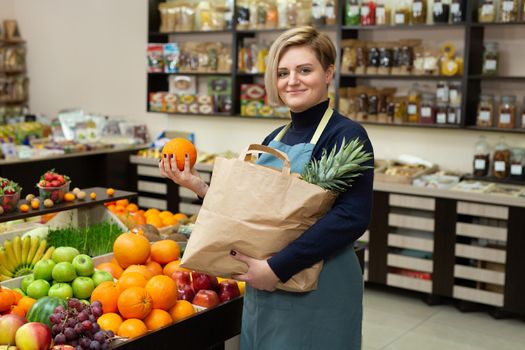 Young saleswoman collects vegetables and fruits in a paper bag