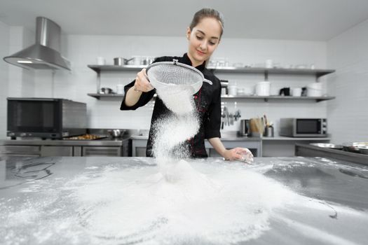 The pastry chef sows the flour through a sieve on the table