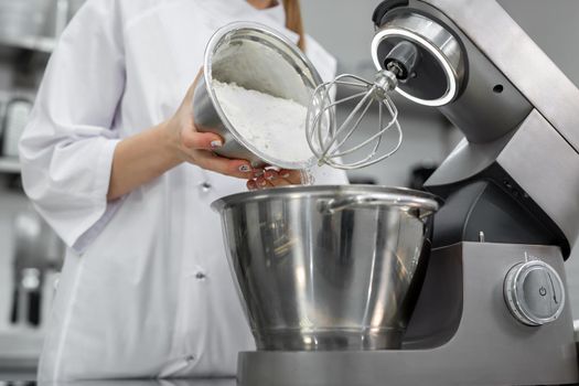 Pastry chef adds flour to the bowl of the mixer