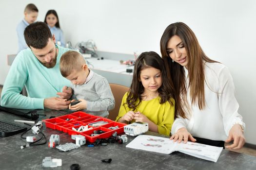 Family with children in a robotics club makes a robot controlled from a constructor