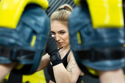 Beautiful girl in boxing gloves hits the paws held by her trainer