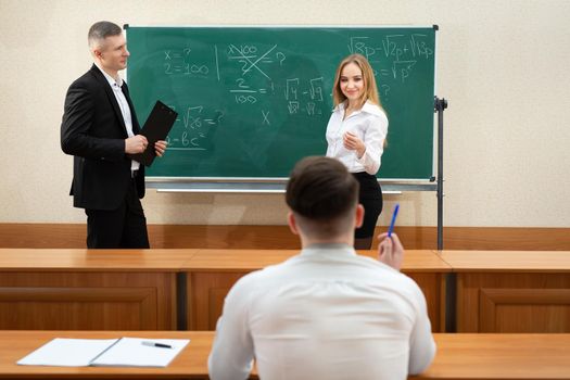 Attractive young female student in a short skirt answers a male teacher near the blackboard