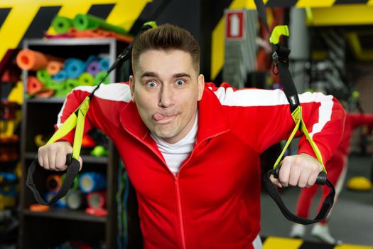 Thin man in a red tracksuit is working out in the gym, having fun and making faces.