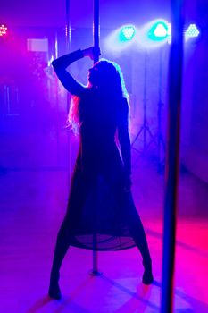 Pole dance. Young slender sexy woman dancing on a pole in the interior of a nightclub with light and smoke