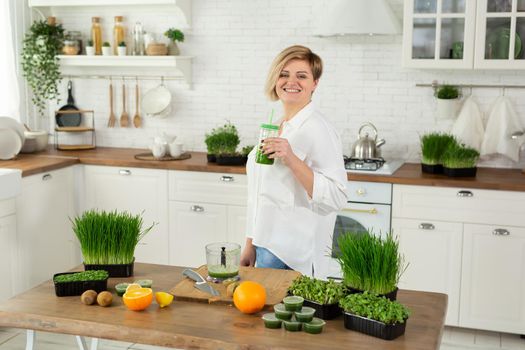 Young beautiful woman drinks a smoothie made from wheat germ juice and micro-greens in the kitchen