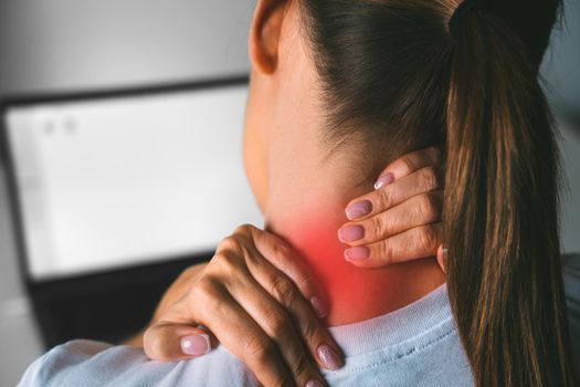 Neck pain after working on computer. Young woman massaging neck to relieve pain after working on pc