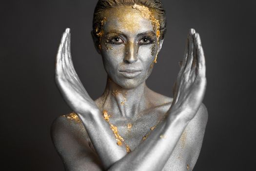Portrait of a beautiful female model with gold and silver paint on her skin and hair in the studio