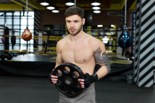 Young muscular guy with a naked torso posing holding a pancake from a barbell.