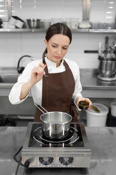 Young female pastry chef adds pistachio paste to the boiling syrup. Cooking dessert in a professional kitchen.