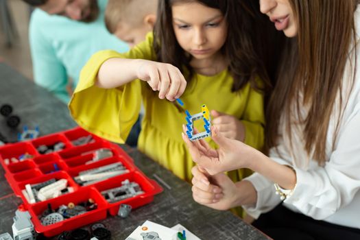 Close-up of a mother and daughter's hands at school making a robot controlled from a construction kit