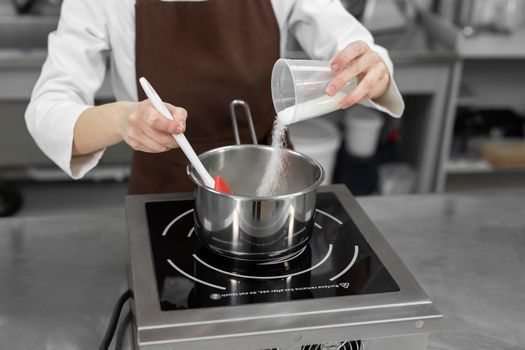 Pastry chef pours the sugar into a saucepan.