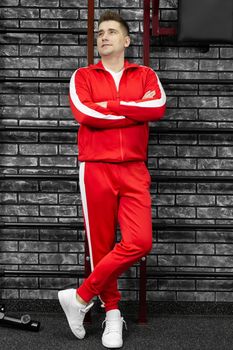 Thin man in a red tracksuit poses against the wall of the gym.