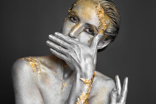 Portrait of a beautiful female model with gold and silver paint on her skin and hair in the studio
