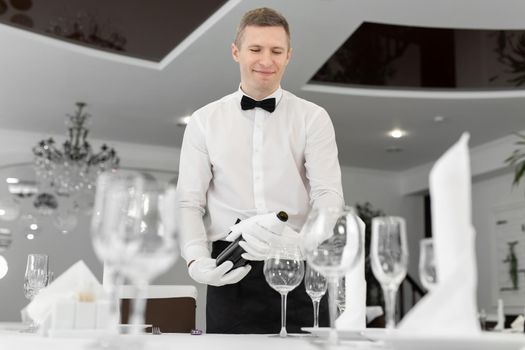 Male waiter in white gloves pours red wine into a glass
