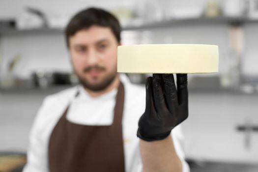 Male pastry chef holds a frozen mousse cake and prepares it for the icing