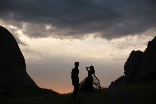 Silhouettes of a young couple lovers at sunset in rays of setting sun